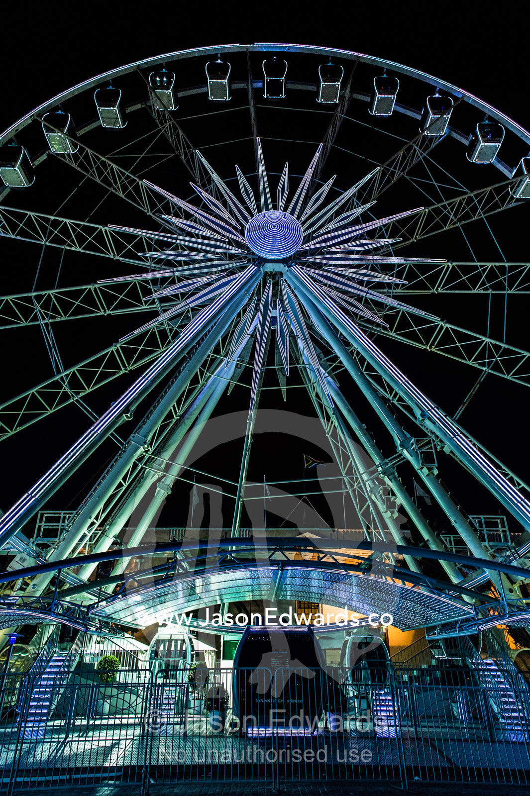 A towering ferris wheel illuminated by neon lights in a marina. Cape Town, Victoria and Alfred Waterfront, Western Cape, South Africa.