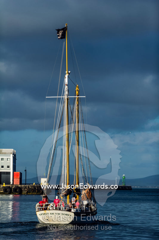 A yacht heads to sea from a harbor flying a pirate flag on it's mast. Cape Town, Victoria and Alfred Waterfront, Western Cape, South Africa.
