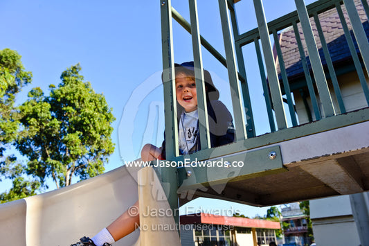 A boy plays on a slide in the playground on his first day of school. Melbourne, Carlton North, Melbourne, Victoria, Australia.