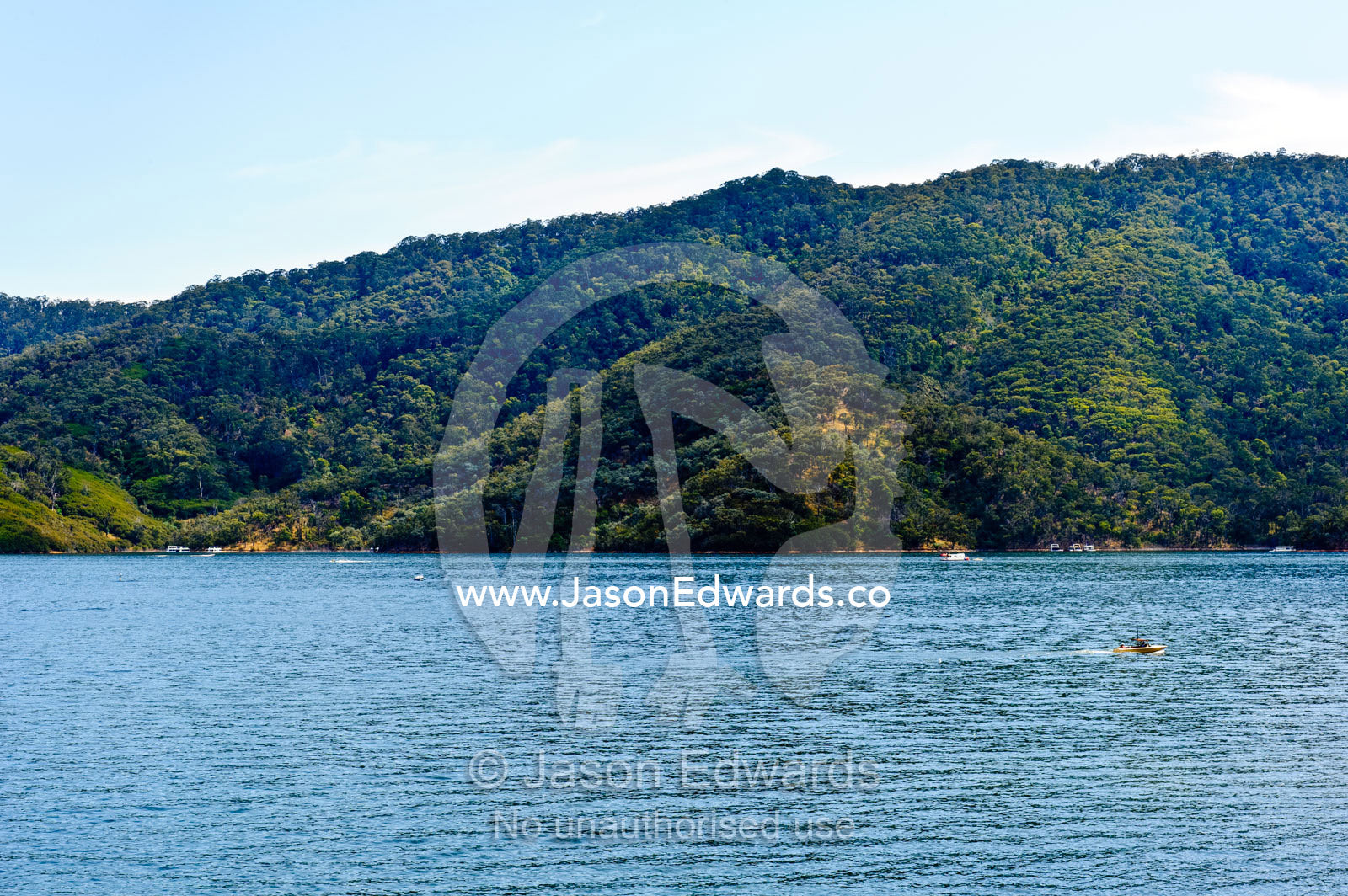 A speed boat on a city water catchment surrounded by forested hills. Lake Eildon, Eildon Weir Spillway, Victoria, Australia.