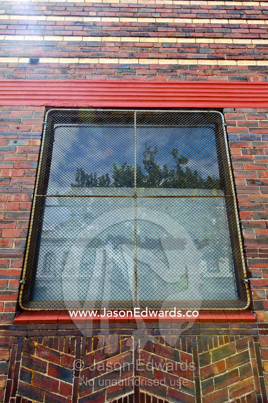 A square window in a red brick wall with a wire security screen. North Melbourne, Melbourne, Victoria, Australia.