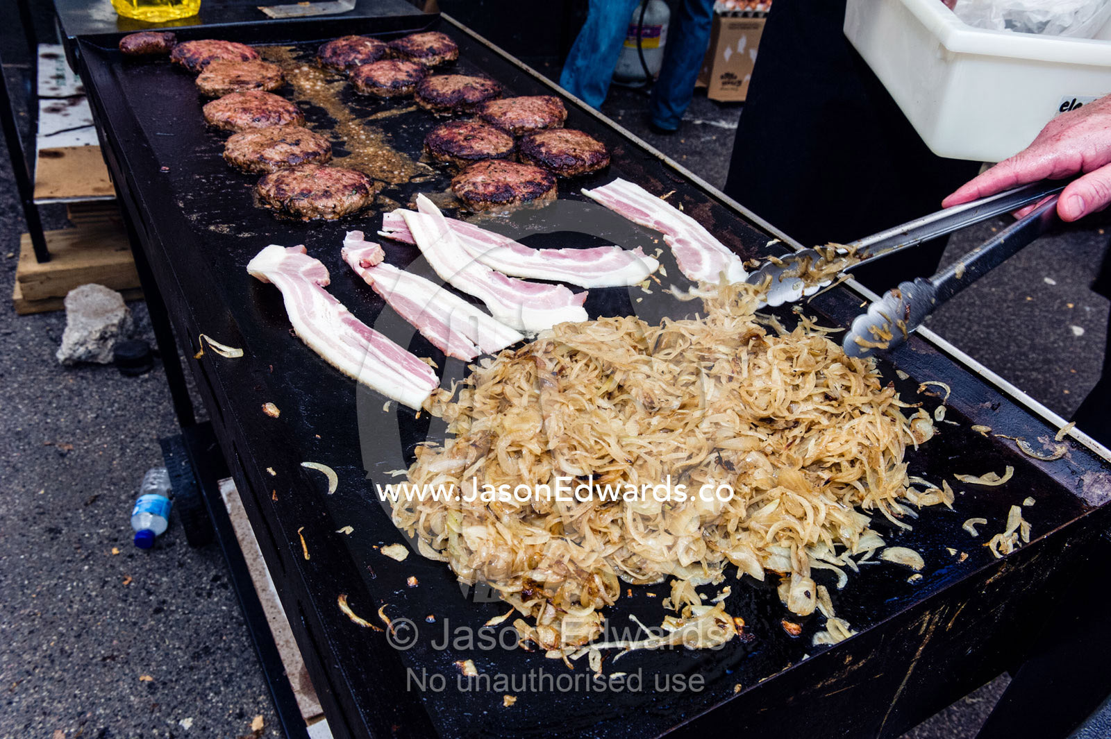Onion, bacon and hamburgers are grilled at a school fete barbecue. Carlton North, Melbourne, Victoria, Australia.