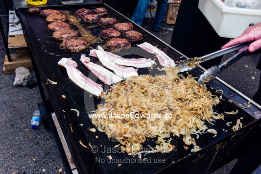 Onion, bacon and hamburgers are grilled at a school fete barbecue. Carlton North, Melbourne, Victoria, Australia.