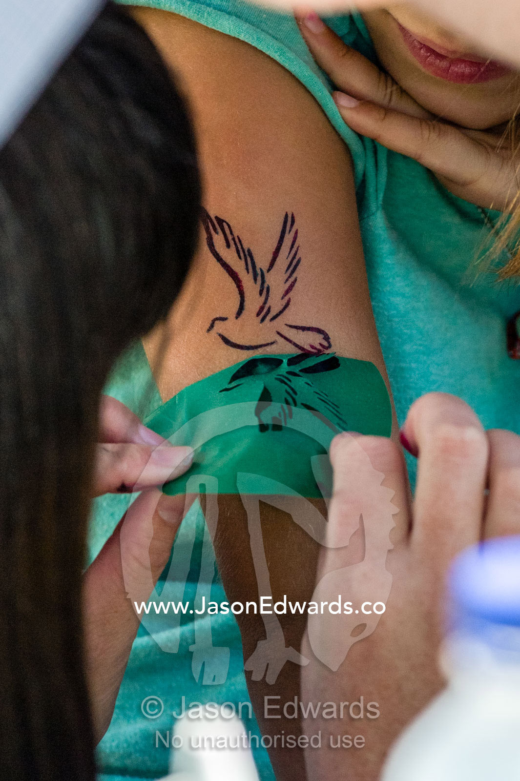 A girl gets a temporary tattoo of a dove at a school fete fundraiser. Carlton North, Melbourne, Victoria, Australia.