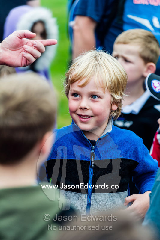An excited young boy listens to the coach at a football training camp. Edinburgh Gardens, Fitzroy North, Melbourne, Victoria, Australia.
