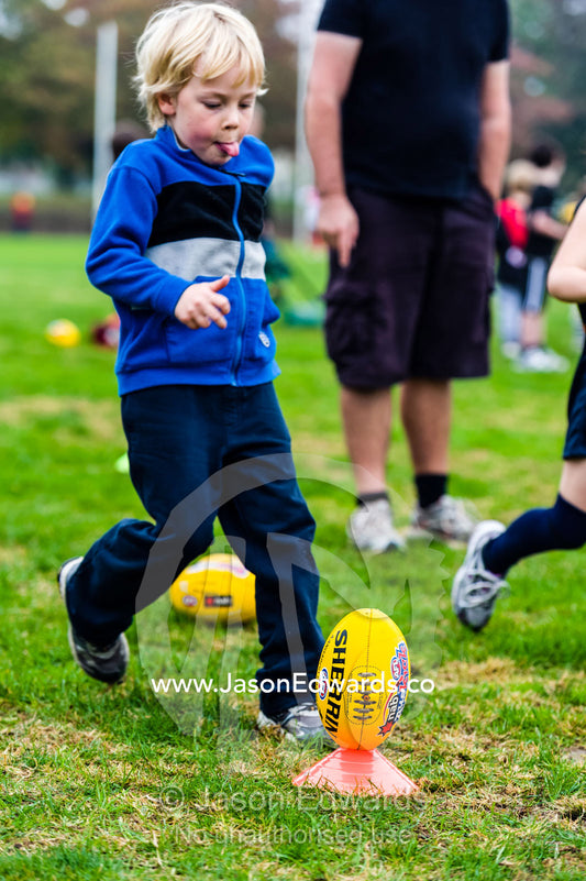 A boy concentrates intently as he practices kicking a football. Edinburgh Gardens, Fitzroy North, Melbourne, Victoria, Australia.