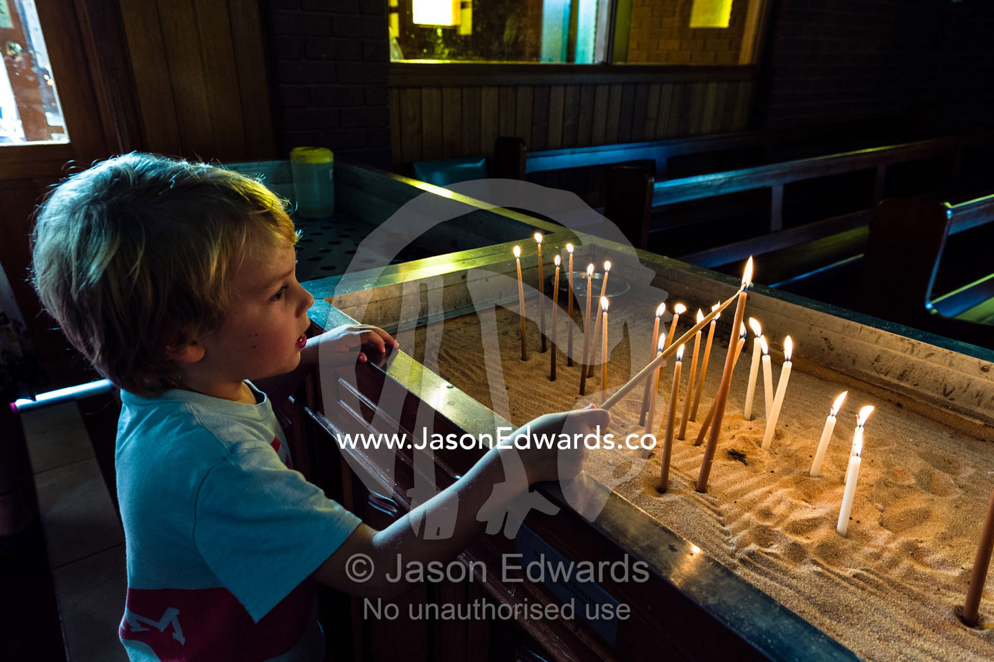 A young boy lights prayer candles in a quiet Greek Orthodox church. St Andrews Greek Orthodox Church, Melbourne, Victoria, Australia.