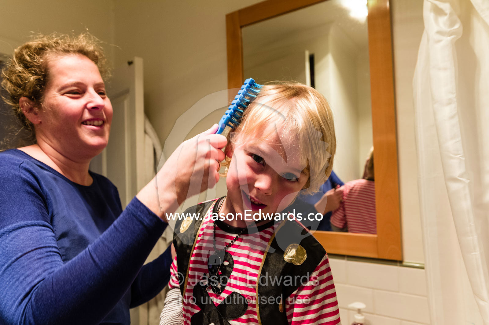 A mother brushes her sons hair as he dresses up as a pirate. Carlton North, Melbourne, Victoria, Australia.
