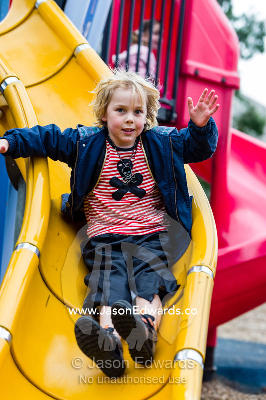 A boy dressed as a pirate slips down a slide in a playground. Birrarung Marr Park, Federation square, Melbourne, Victoria, Australia.