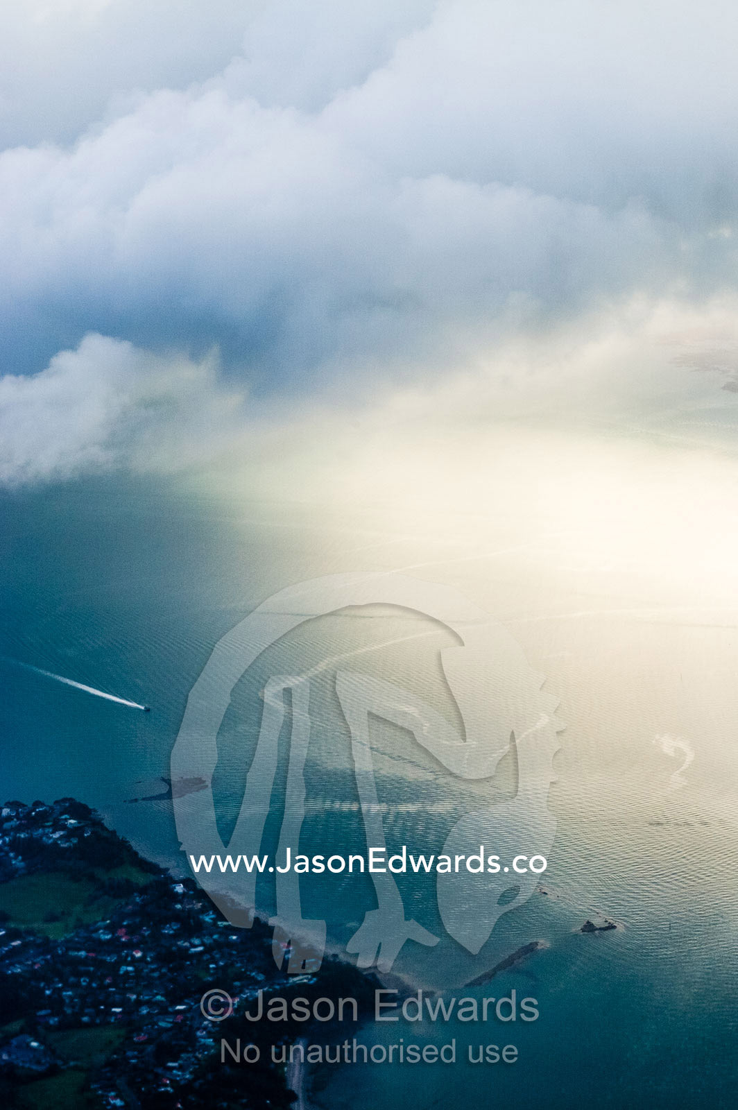 Sunlight pierces a storm over the ocean and boat at high speed. Auckland, New Zealand.