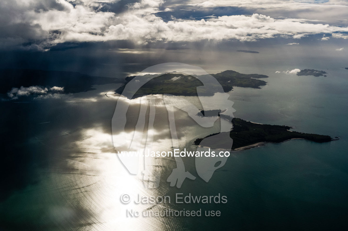 Sunrays pierce a dark and brooding storm over a bay of islands. Auckland, New Zealand.