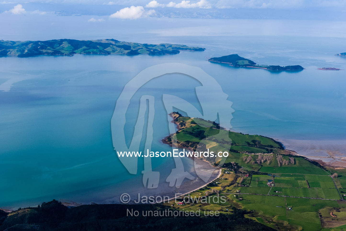 A peninsular dotted with lush farmland fingers into a turquoise bay. Auckland, New Zealand.