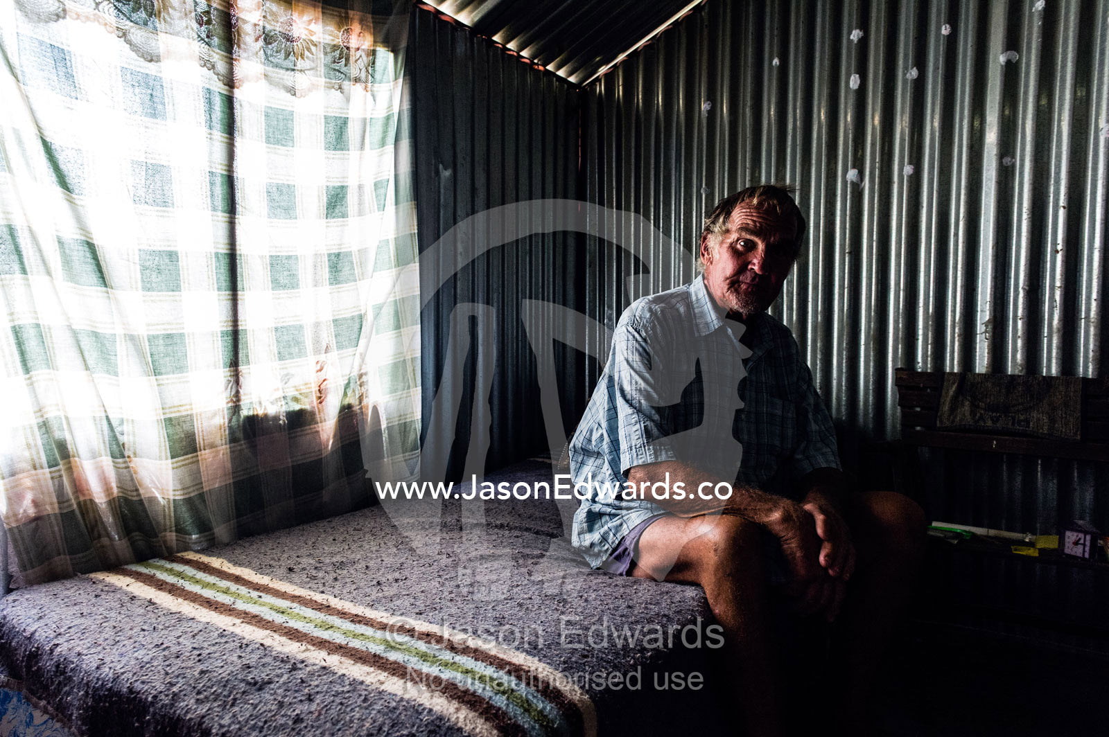 A man sits inside a corrugated tin garden shed that is his home. Bon Accord Dam, Gauteng Province, South Africa.