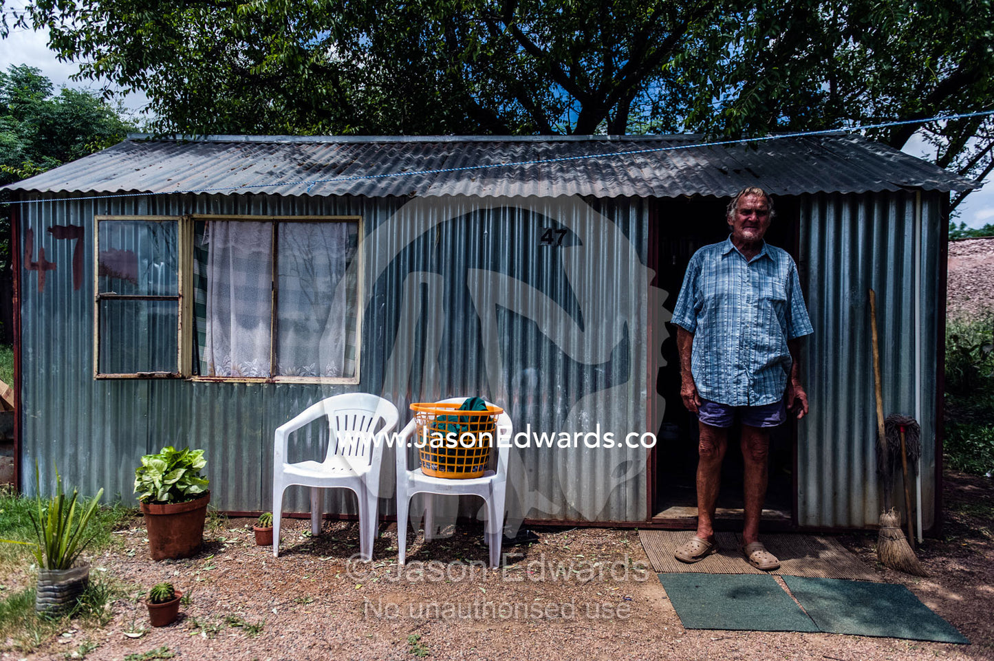 A man stands outside a corrugated tin garden shed that is his home. Bon Accord Dam, Gauteng Province, South Africa.