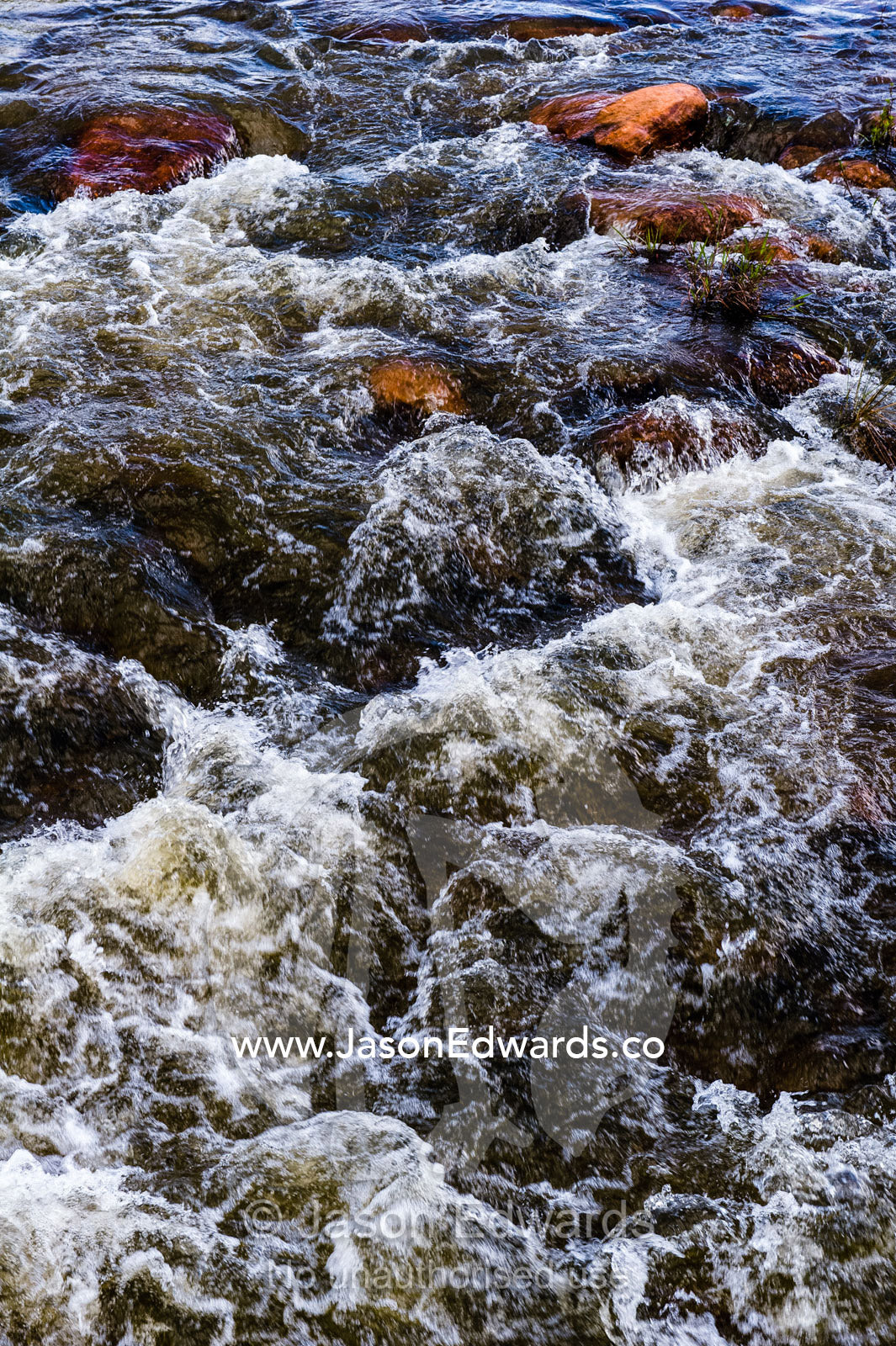 Water cascades and foams as it flows over boulders in a small river. Waterberg Mountains, Entabeni Game Reserve, Limpopo Province, South Africa.