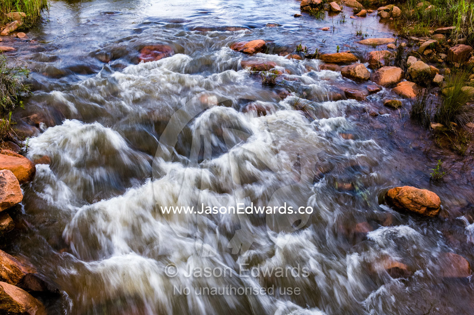 Water cascades and foams as it flows over boulders in a small river. Waterberg Mountains, Entabeni Game Reserve, Limpopo Province, South Africa.