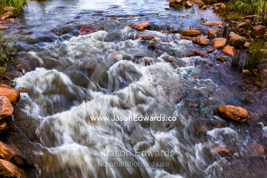 Water cascades and foams as it flows over boulders in a small river. Waterberg Mountains, Entabeni Game Reserve, Limpopo Province, South Africa.