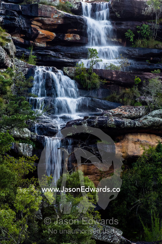 A waterfall cascading down a rocky forest escarpment. Waterberg Mountains, Entabeni Game Reserve, Limpopo Province, South Africa.