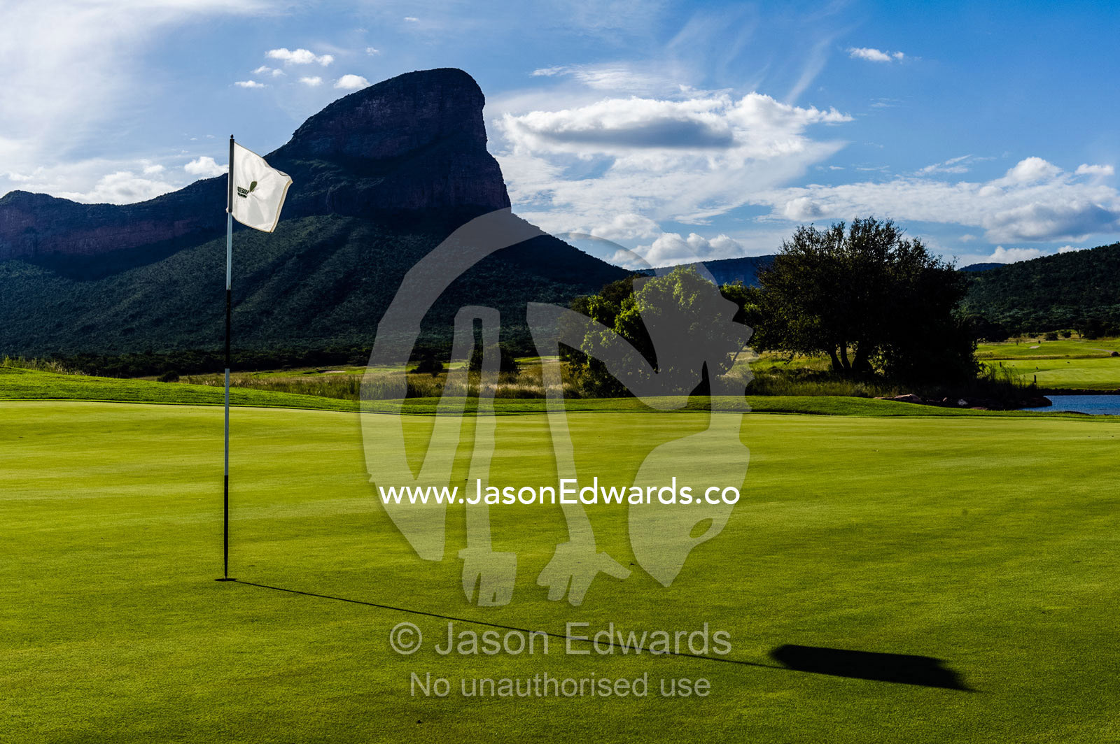 A flag rests in the cup on a golf green beneath rugged mountain peaks. Legend Golf Safari Resort, Waterberg Mountains, Entabeni Game Reserve, Limpopo Province, South Africa.