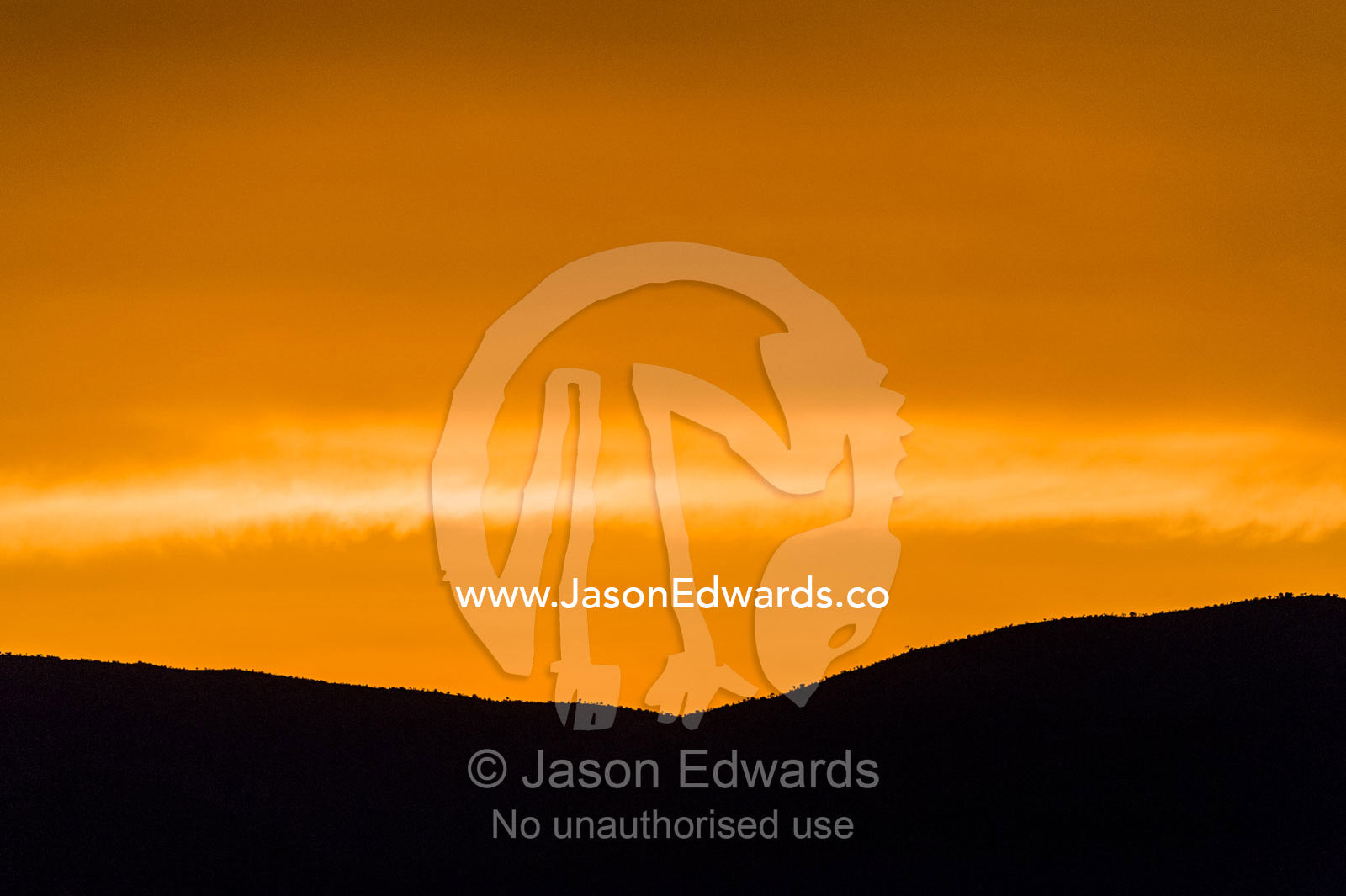 An orange sunset afterglow over a silhouette of a mountain ridge line. Waterberg Mountains, Entabeni Game Reserve, Limpopo Province, South Africa.
