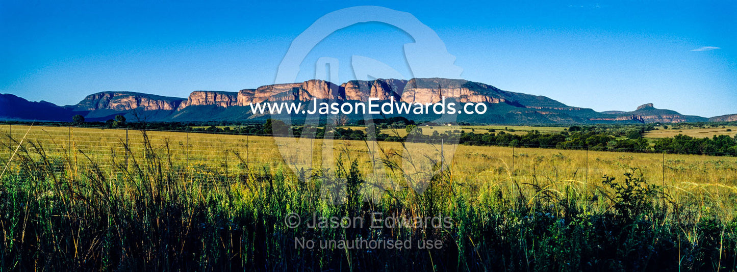 Dawn illuminates the cliffs of a mountain range overlooking farmland. Waterberg Mountains, Entabeni Game Reserve, Limpopo Province, South Africa.
