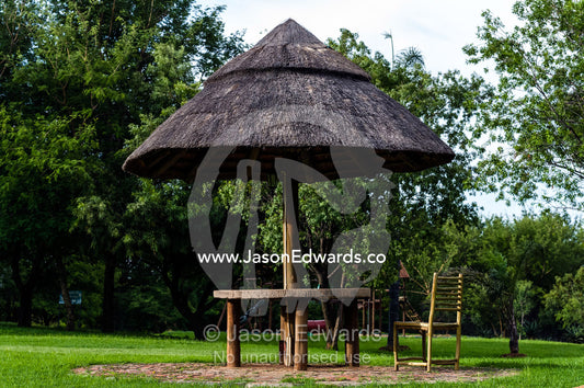 A thatched roof over a picnic table in the garden of a safari lodge. The Farm Inn, Pretoria, Gauteng Province, South Africa.