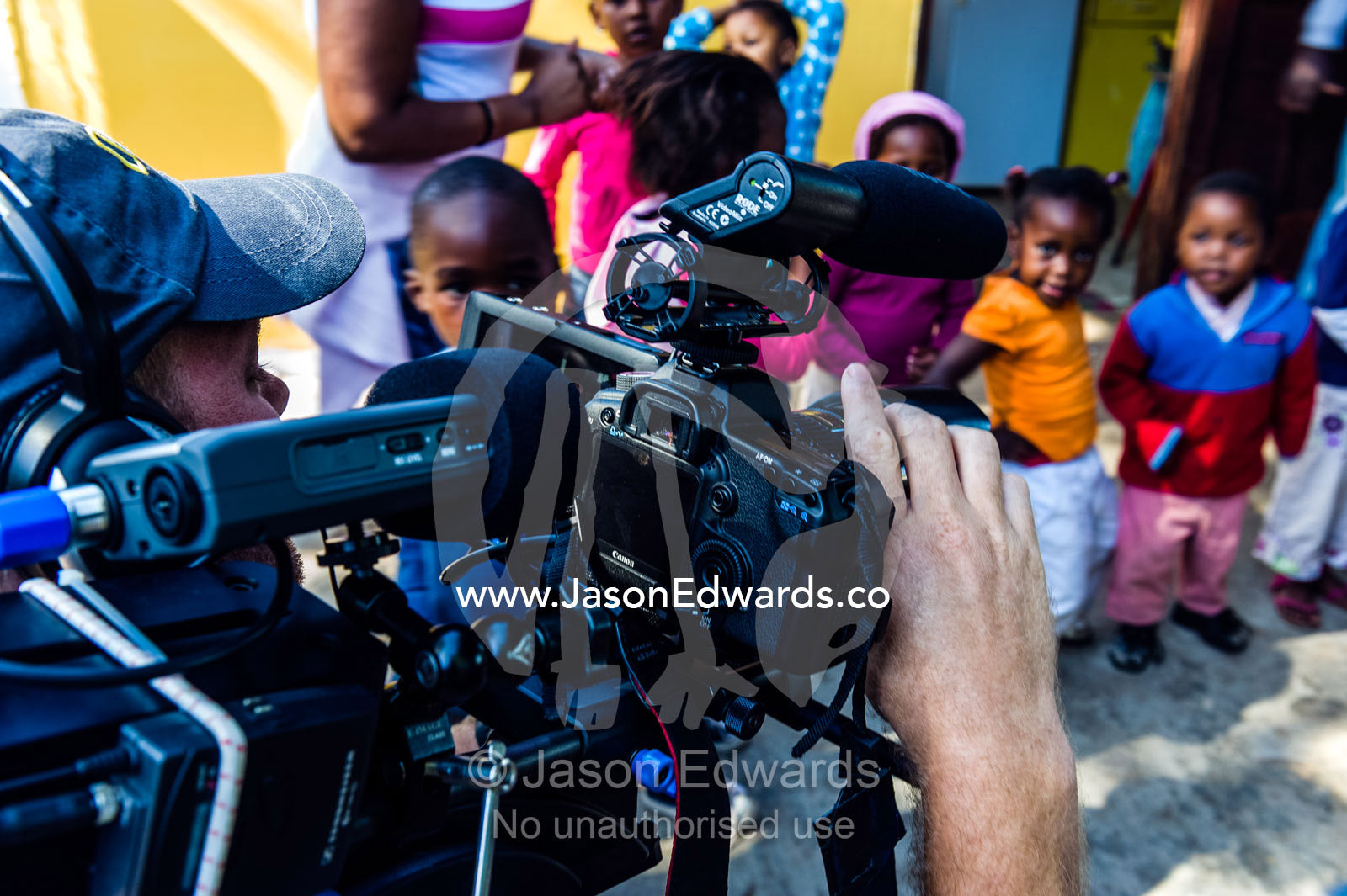 A cameraman filming African refugee children playing at a pre-school. Red Hill Township and Pre-School, Cape Town, Western Cape, South Africa.