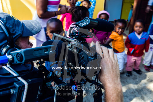 A cameraman filming African refugee children playing at a pre-school. Red Hill Township and Pre-School, Cape Town, Western Cape, South Africa.