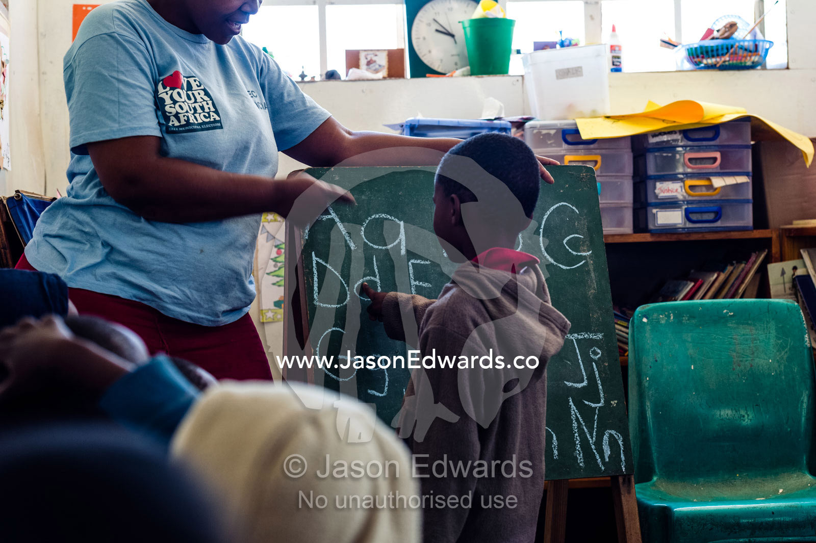 A teacher helps a student with the letters of the alphabet at school. Red Hill Township and Pre-School, Cape Town, Western Cape, South Africa.