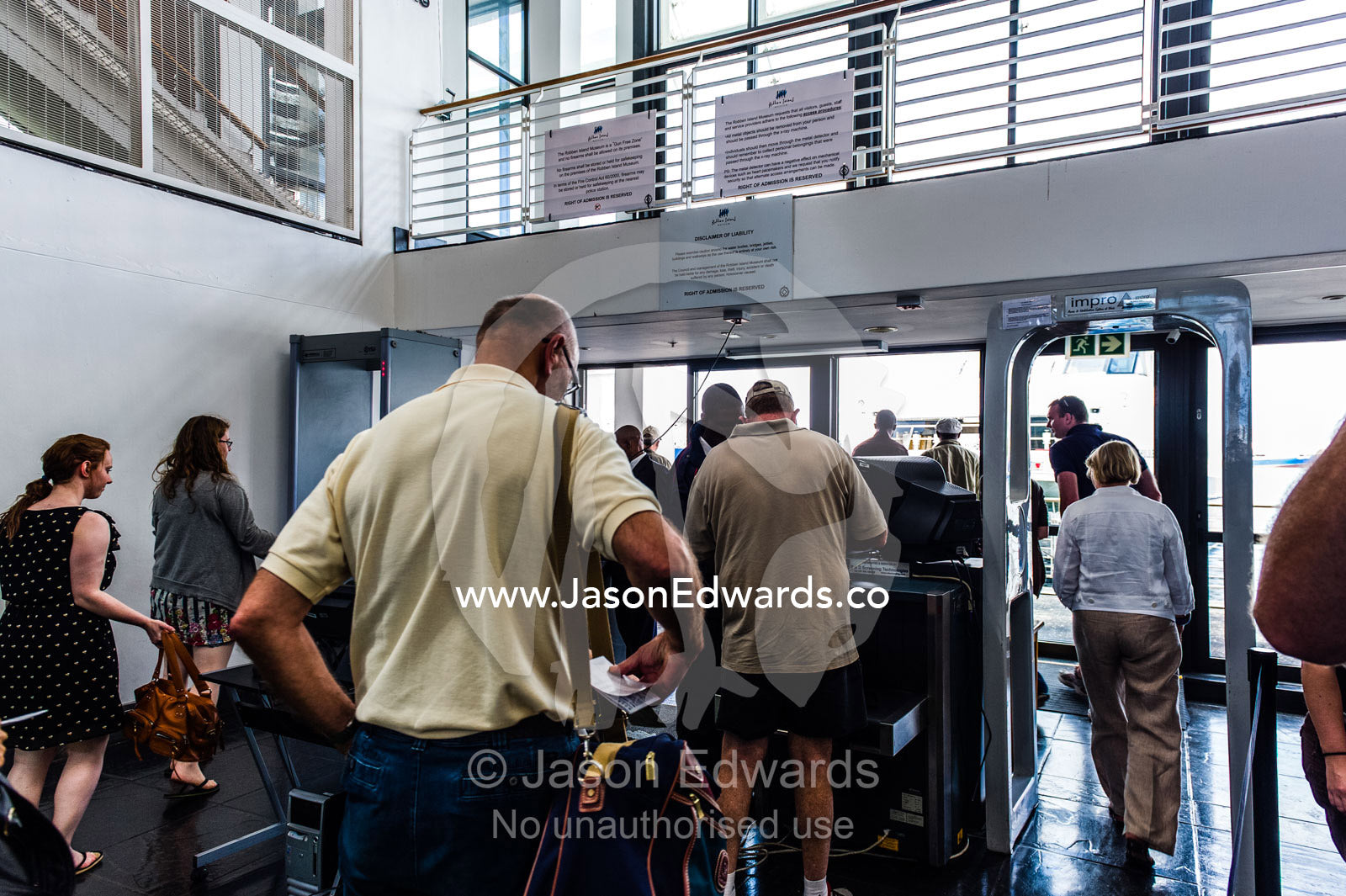 Tourists queue at a security check point to board a passenger ferry. Robben Island, Cape Town, Bloubergstrand, Table Bay, Western Cape, South Africa.