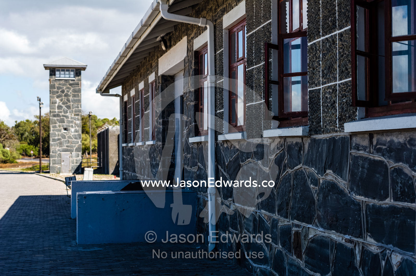 A prison wall patrolled by a bluestone guard tower. Cape Town, Robben Island, Bloubergstrand, Table Bay, Western Cape, South Africa.