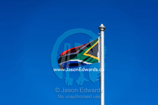 The South African flag fluttering in a clear blue sky above a prison. Cape Town, Robben Island, Bloubergstrand, Table Bay, Western Cape, South Africa.