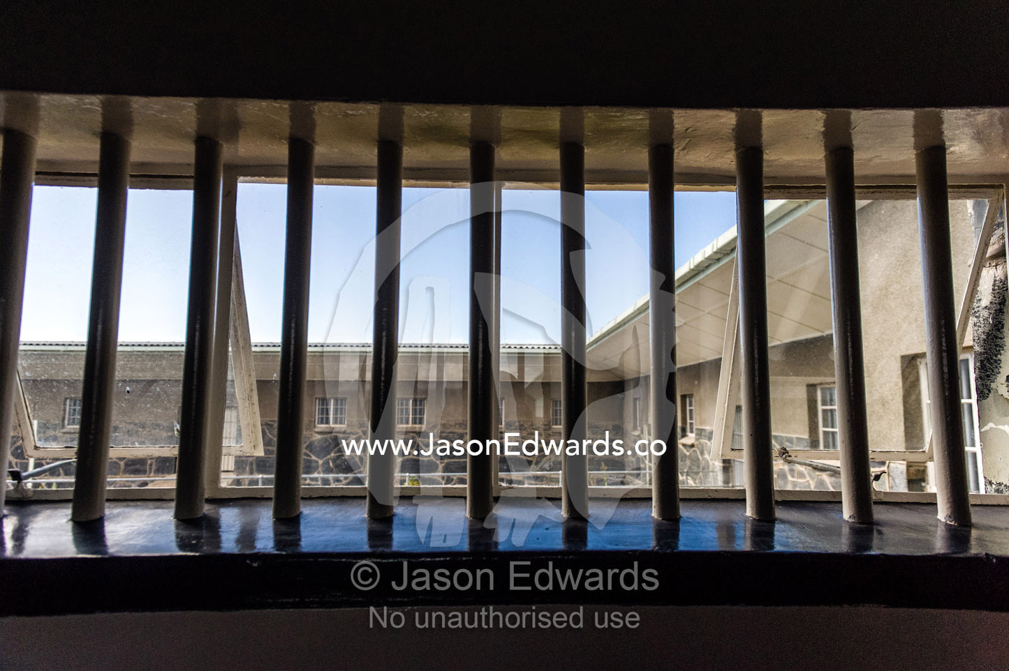 Looking through prison bars to an exercise yard and blue sky. Robben Island, Cape Town, Bloubergstrand, Table Bay, Western Cape, South Africa.