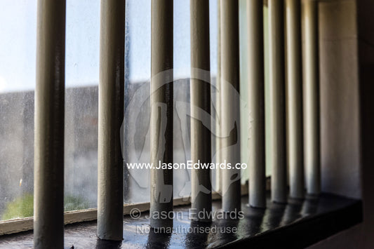 Sunlight catches stout steel bars in a prison cell. Robben Island, Cape Town, Bloubergstrand, Table Bay, Western Cape, South Africa.