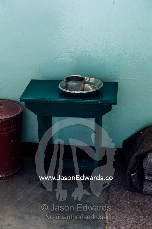A table holds a cup and bowl in the cell inhabited by Nelson Mandela. Robben Island, Cape Town, Bloubergstrand, Table Bay, Western Cape, South Africa.