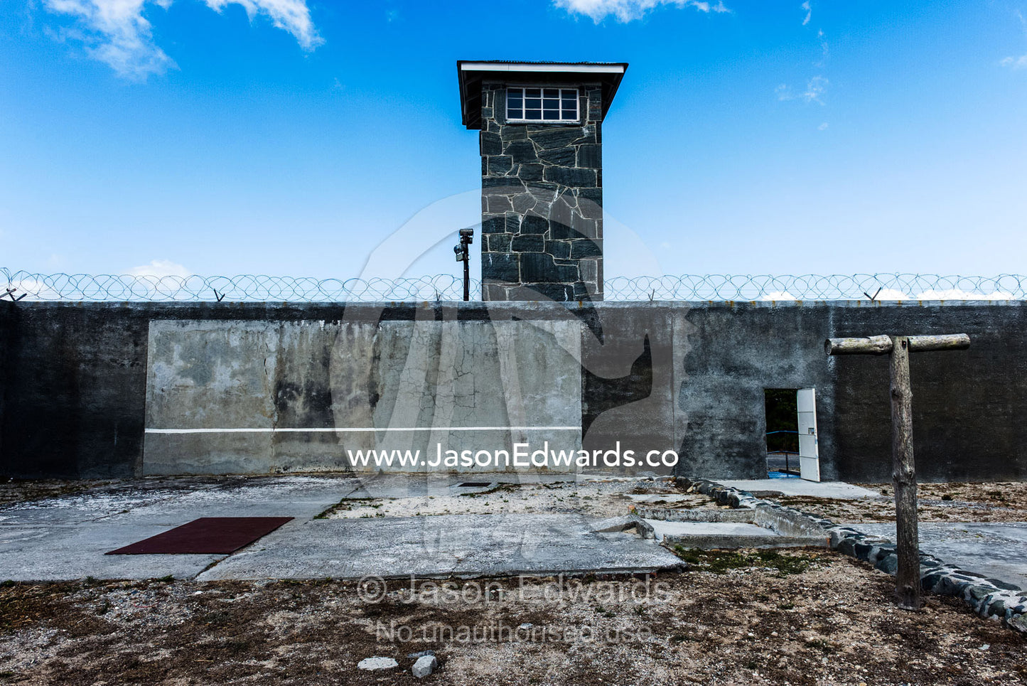 A guard tower overlooks cold grey prison yard and barbwire wall. Robben Island, Cape Town, Bloubergstrand, Table Bay, Western Cape, South Africa.