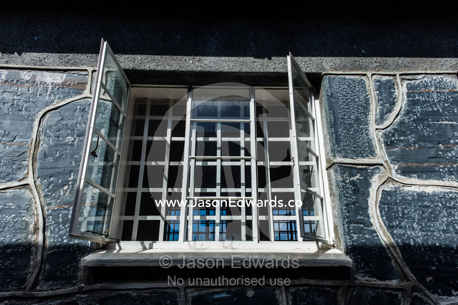 Steel bars enclose a window in a grey stone prison wall. Robben Island, Cape Town, Bloubergstrand, Table Bay, Western Cape, South Africa.