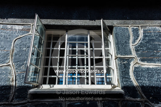 Steel bars enclose a window in a grey stone prison wall. Robben Island, Cape Town, Bloubergstrand, Table Bay, Western Cape, South Africa.