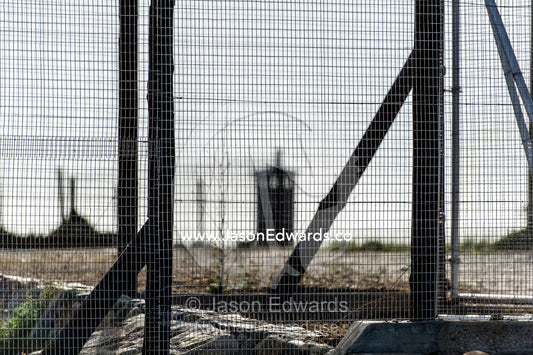 Rows of steel and wire mesh fencing surround a prison and guard tower. Robben Island, Cape Town, Bloubergstrand, Table Bay, Western Cape, South Africa.