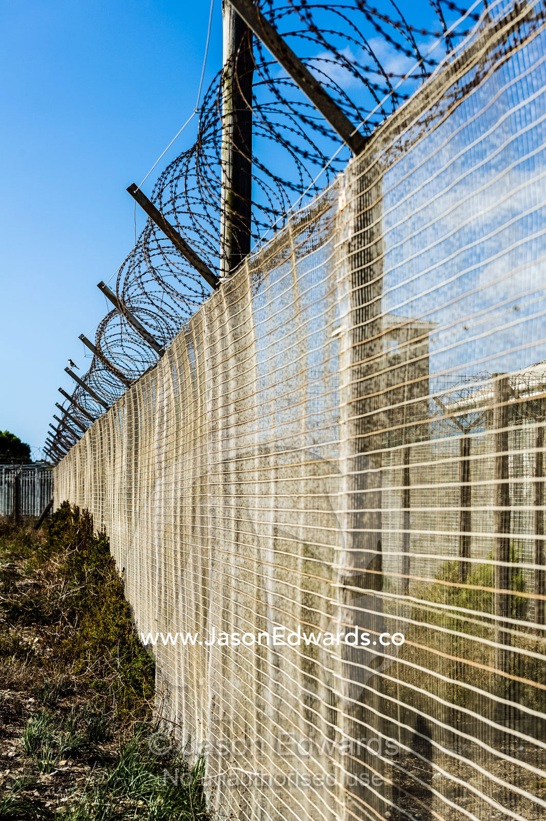 A steel and wire mesh fence topped with razor wire surrounds a prison. Robben Island, Cape Town, Bloubergstrand, Table Bay, Western Cape, South Africa.