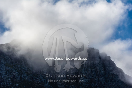 Clouds and fog shroud the summit of a sheer coastal mountain range. Cape Town, Chapmans Peak Drive, Chapmans Peak, Western Cape, Cape Peninsula, South Africa.