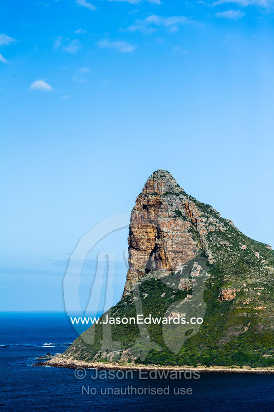 A rugged mountain peak soars into the sky and spears into the ocean. Sentinel Peak, Hout Bay, Cape Town, Chapmans Peak Drive, Western Cape, Cape Peninsula, South Africa.