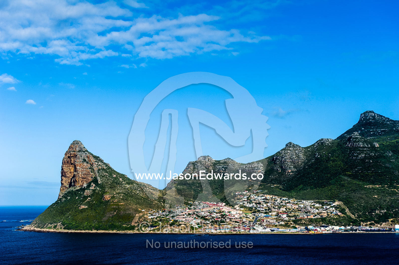 A coastal community nestled in a sheltered bay beneath mountain peaks. Sentinel Peak, Hout Bay, Cape Town, Chapmans Peak Drive, Western Cape, Cape Peninsula, South Africa.
