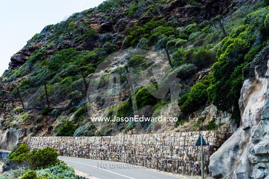 Wire mesh netting catches boulders that fall from a cliff onto a road. Cape Town, Chapmans Peak Drive, Chapmans Peak, Western Cape, Cape Peninsula, South Africa.