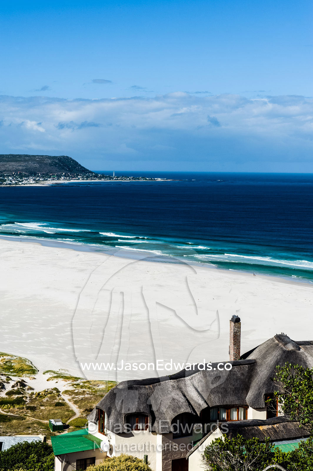 The thatched roof of a house overlooking the ocean and a white beach. Noordhoek Beach, Cape Town, Chapmans Peak Drive, Western Cape, South Africa.