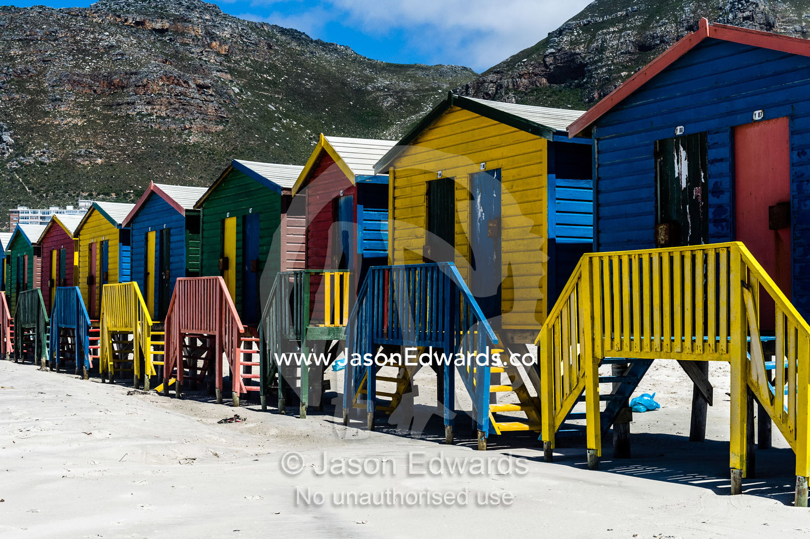 Brightly painted bathing boxes on stilts on the beach in summer. Surfers Corner, Muizenberg, Cape Town, Chapmans Peak Drive, Western Cape, South Africa.