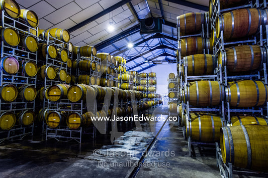 Racks holding rows of wine barrels in a winery storage warehouse. Fairview Wine Estate, Stellenbosch, Western Cape, South Africa.