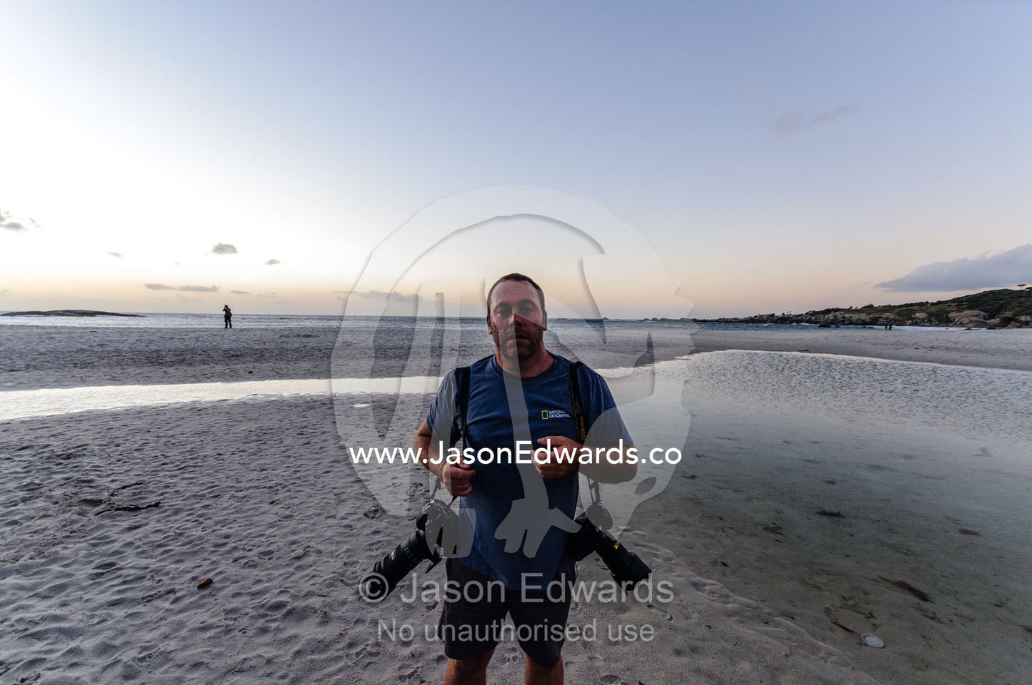 Photographer Jason Edwards filming on a wide low tide beach at sunset. Clifton Beach, Cape Town, Western Cape, South Africa.