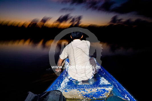 A villager paddles a tin canoe across an Amazonian lake as darkness falls across the rainforest. Quistococha Lake, Lago de Quistococha, Parque de Quistococha, Quistococha Zoo, Iquitos, Amazon Basin, Loreto Region, Maynas Province, Peru.