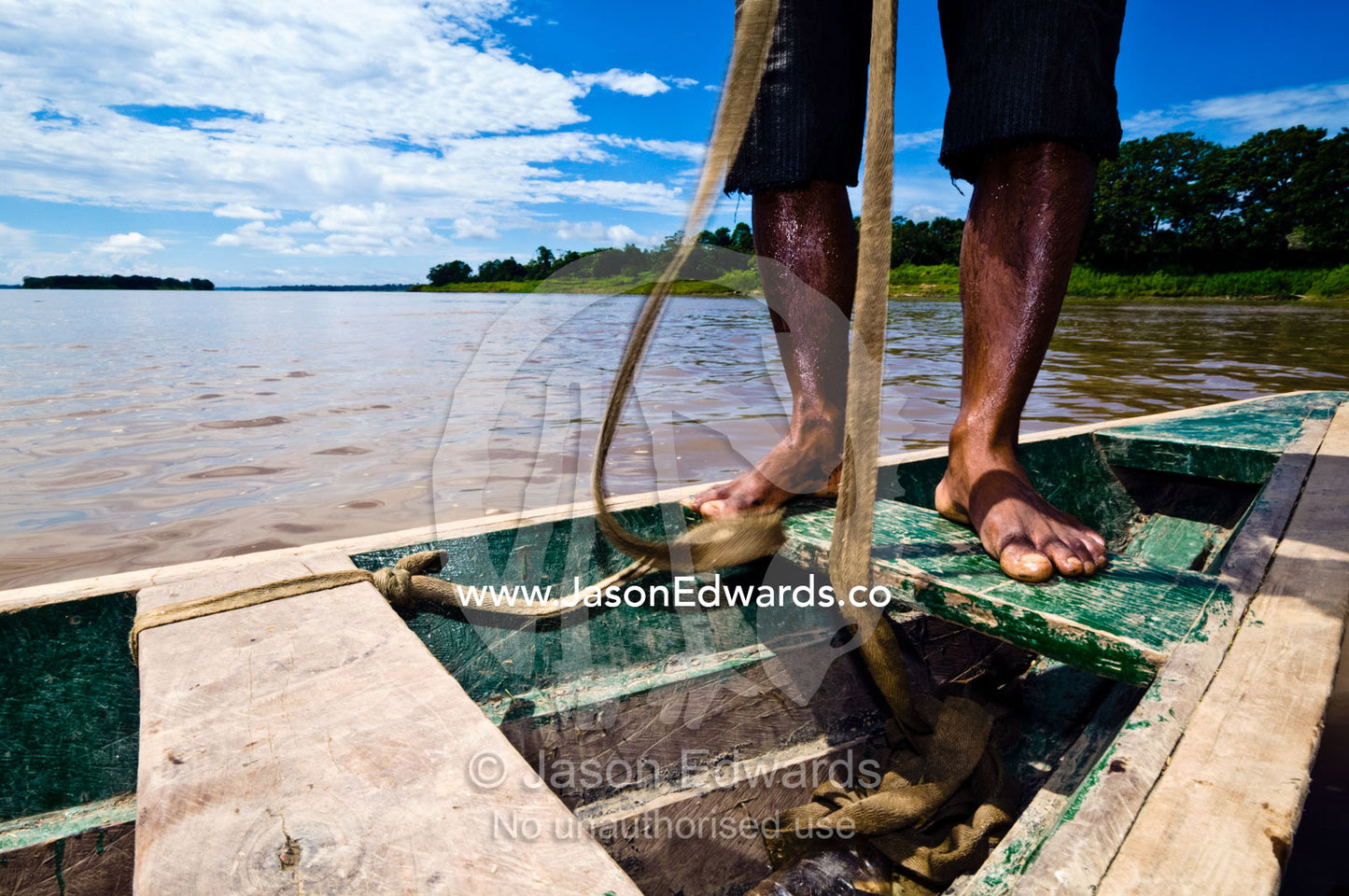 A boatman from an Amazon River village standing on the deck of his fishing boat tying ropes. Amazon River, Rio Amazonas, Amazon Basin, Loreto Region, Maynas Province, Peru.